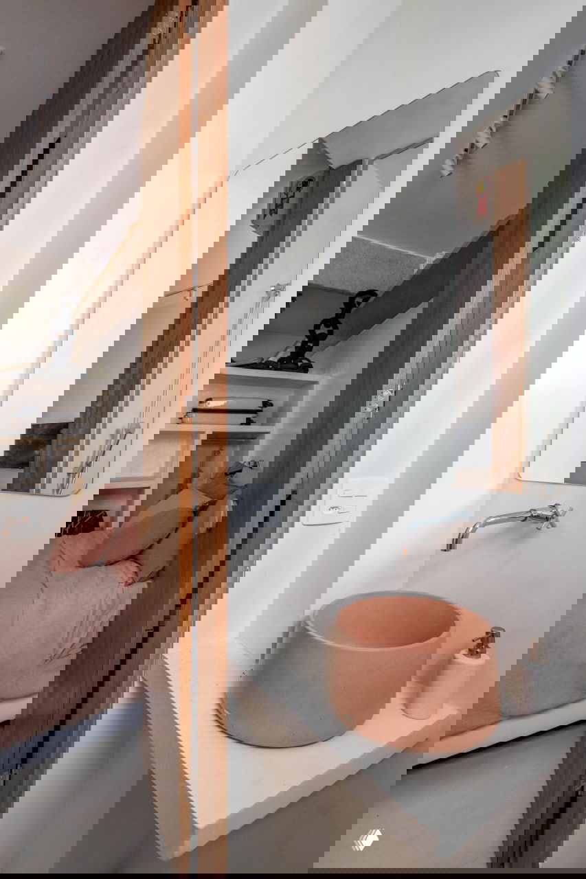 Малый санитарный уголок рядом со спальной зоной: терракотовая круглая раковина на бетонной полке, простое зеркало и деревянная дверь в интерьерном акценте.