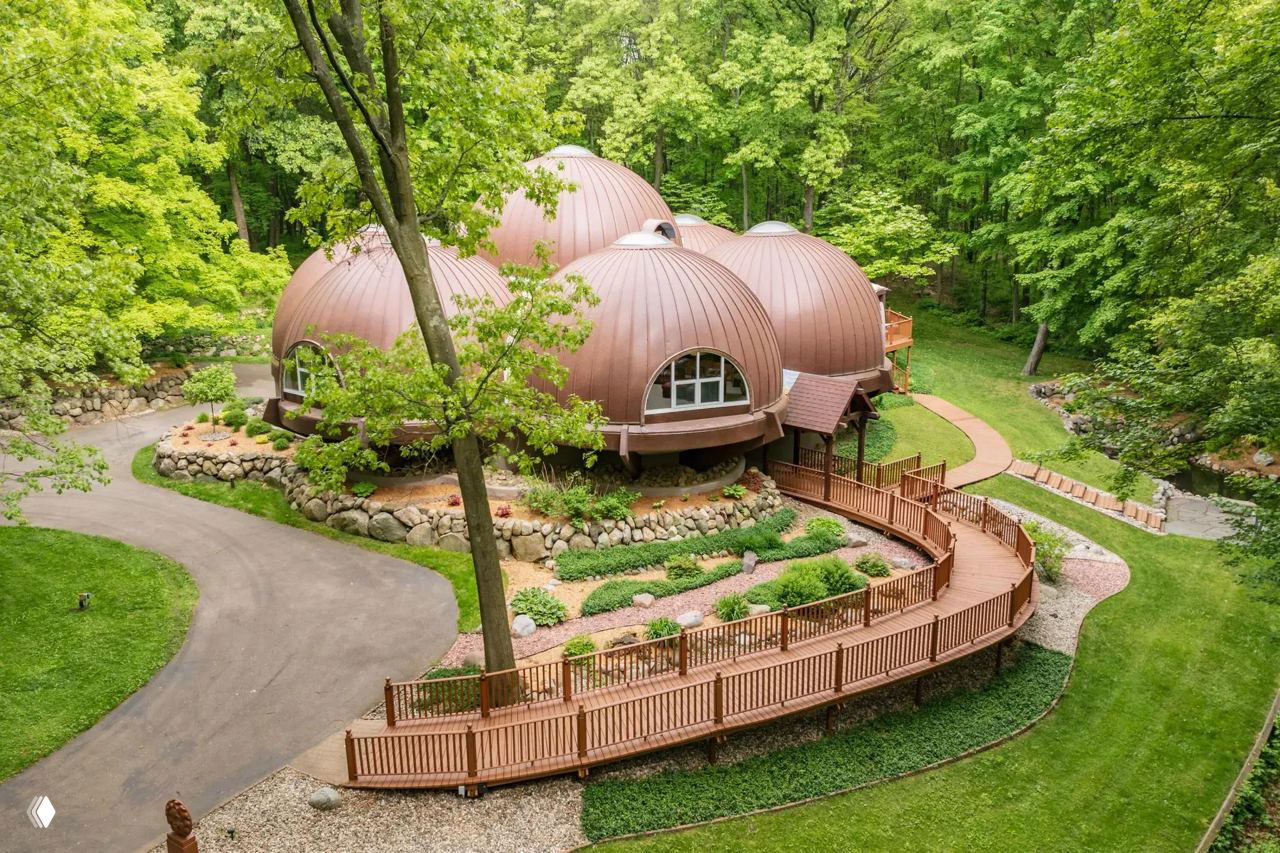 Боковой ракурс здания: куполообразные структуры на фундаменте, ограждение деревянной дорожки и тщательно оформленные газоны вокруг дома.