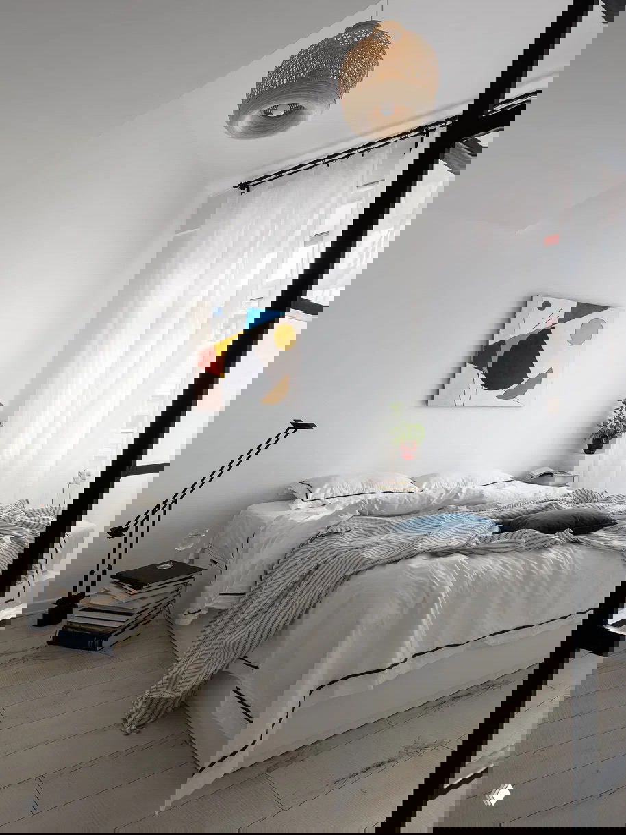 Минималистичная спальня в светлых тонах: низкая кровать, большие окна с прозрачными шторами и минимум мебели для ощущения простора и воздуха.