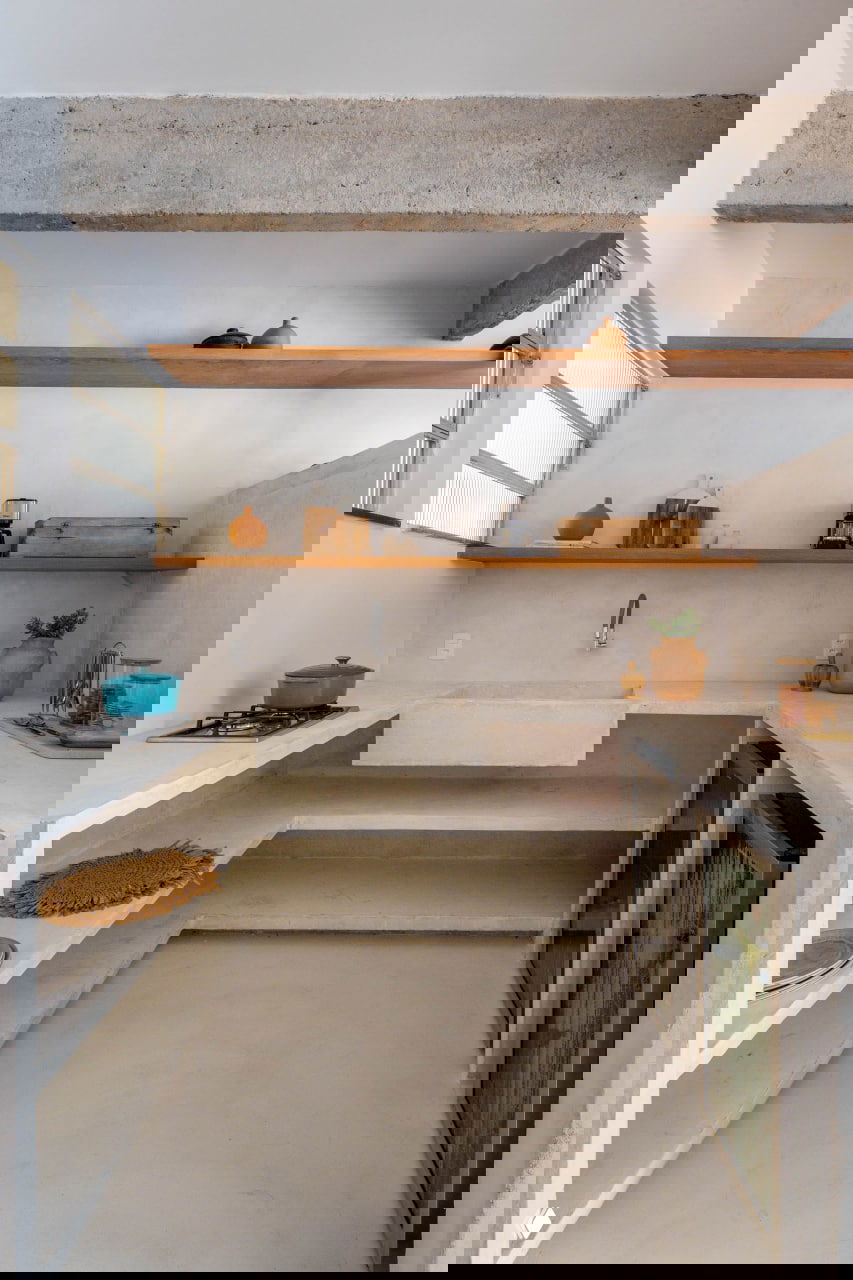 Минималистичная кухня с бетонной рабочей поверхностью и встроенной мойкой, открытые деревянные полки и минимальный набор кухонной утвари.