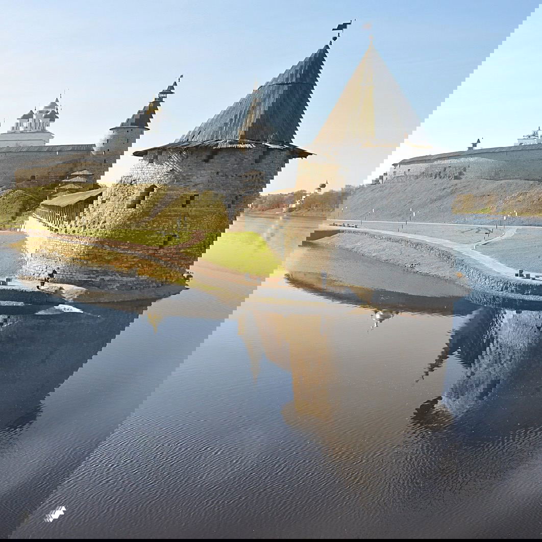 Псковский кремль у воды: крепостная башня и гладкая поверхность реки с отражением белых стен и собора.