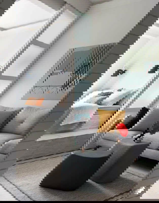 Небольшая гостиная с светло‑серым диваном, низкими пуфиками и открытым переходом в спальную зону — пример рационального зонирования маленькой квартиры.