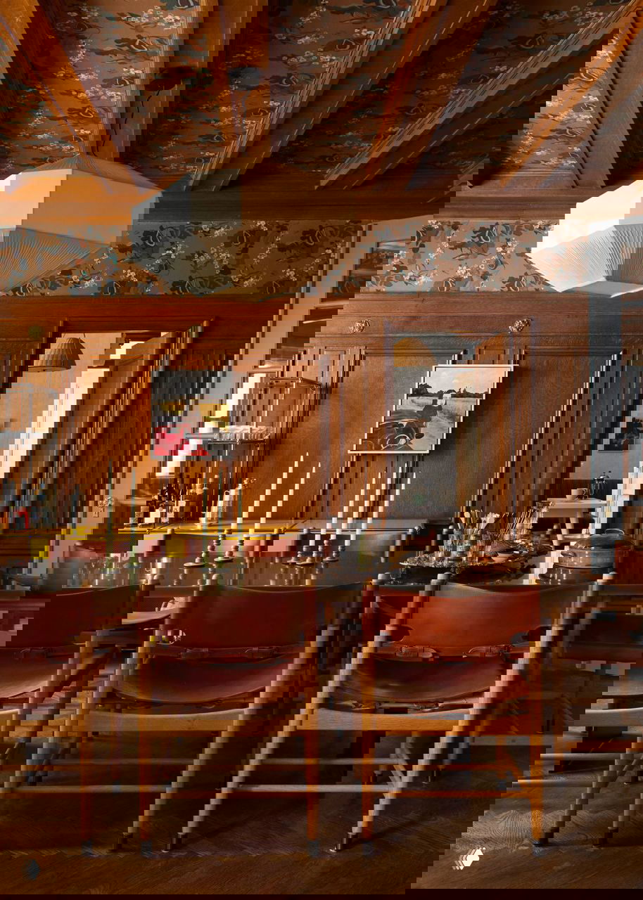 Дубовая столовая с длинным тёмным столом, кожаными стульями и декоративным потолком — тёплая насыщенная атмосфера интерьера.