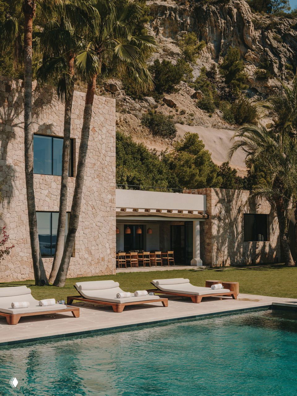 Пляжная зона виллы у бассейна с лежаками на фоне каменного фасада и скалистого рельефа — сочетание природы и минималистской архитектуры.