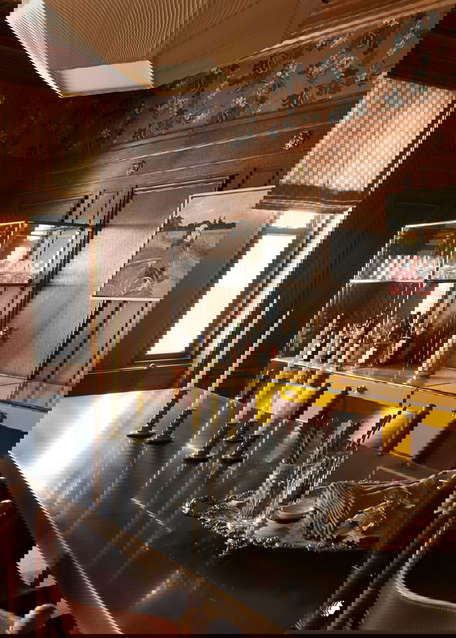 Стол с высокими подсвечниками на фоне шкафов и яркого канареечно‑жёлтого комода; отражения и текстуры в деталях столовой.