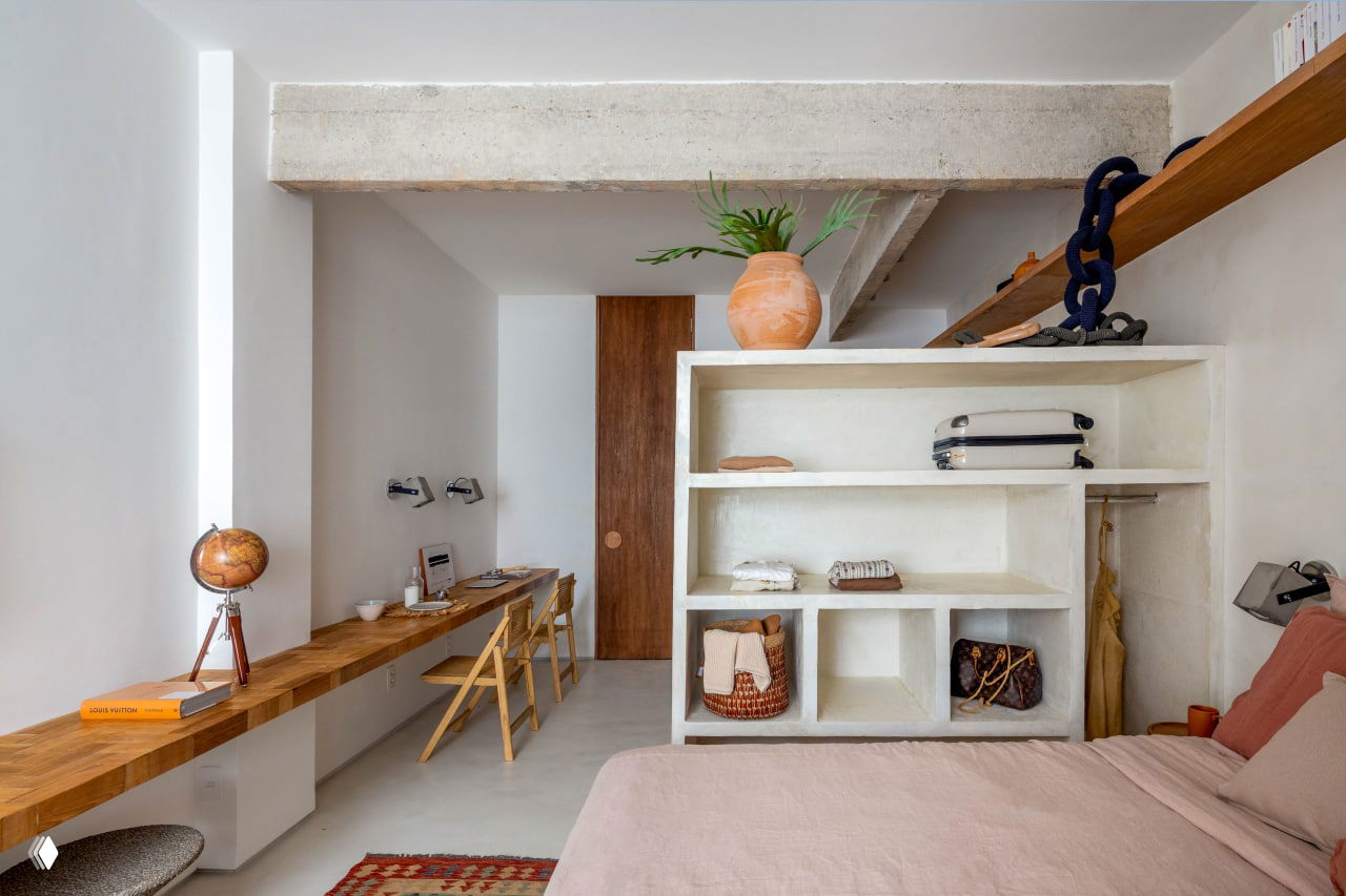 Открытая стеллажная перегородка из белого бетона, деревянная рабочая столешница с плетёными корзинами и декоративными элементами на полках.