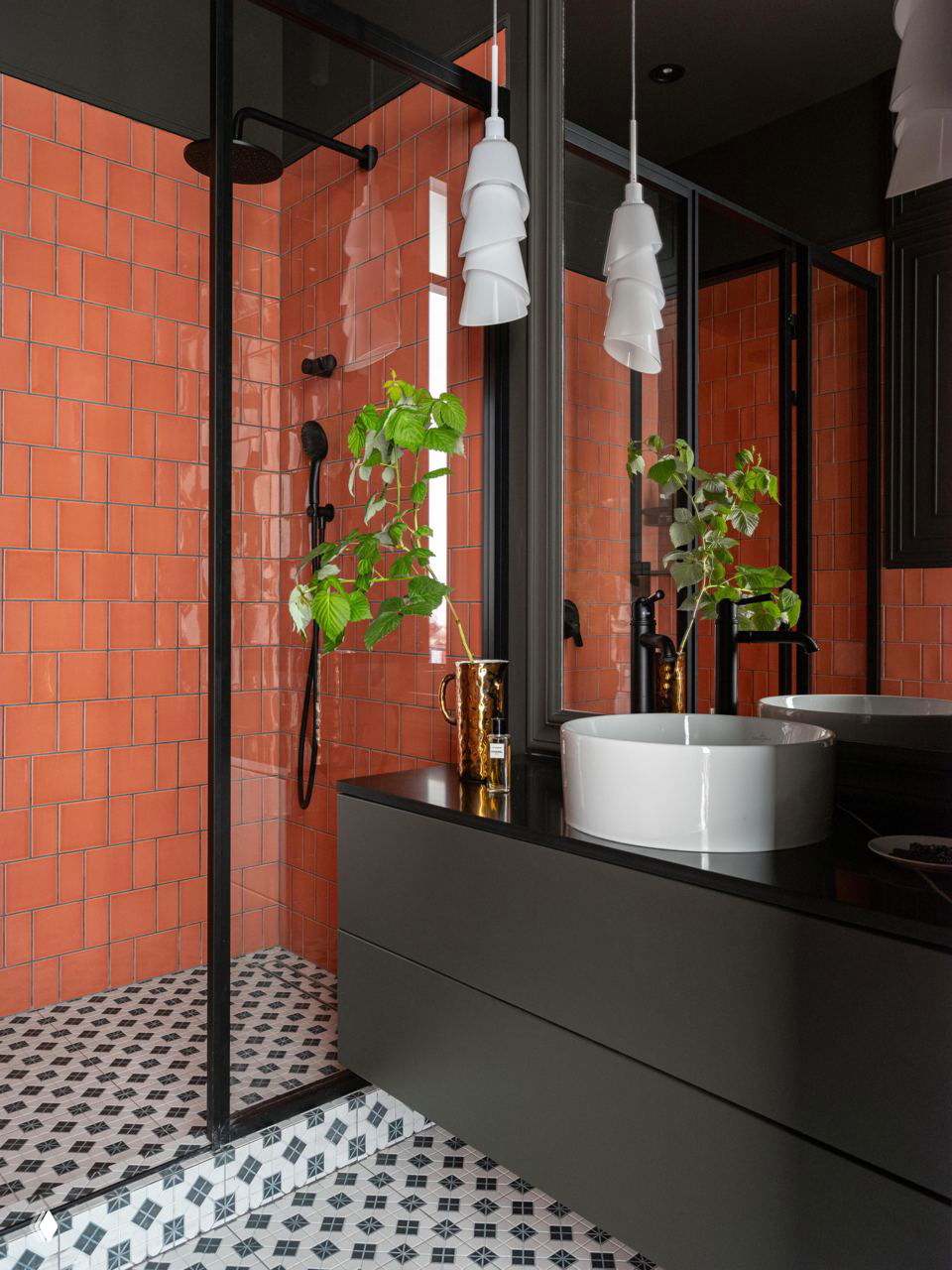 Ванная комната с яркой коралловой плиткой в душевой, чёрной мебелью под раковиной и декоративными керамическими элементами на столешнице.