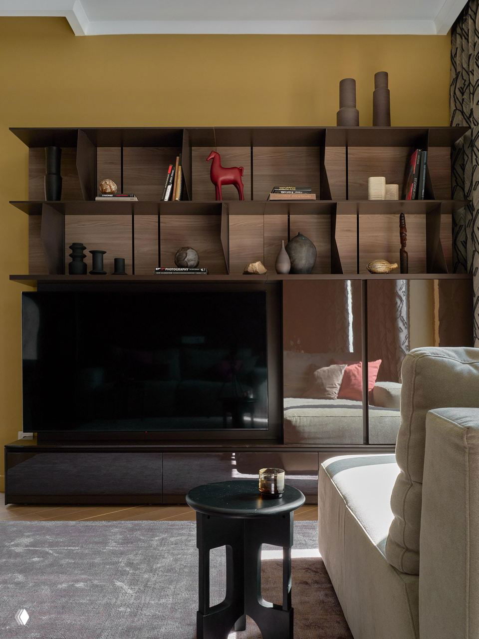 Гостиная: модульная полка с предметами декора и низкая тумба под телевизор, сочетание матовых и глянцевых поверхностей на фоне горчичных стен.