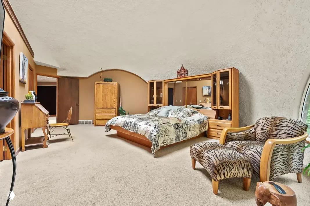 Главная спальня с мягким ковровым покрытием, мебелью из светлого дерева и округлым контуром потолка — спальня под верхним куполом.