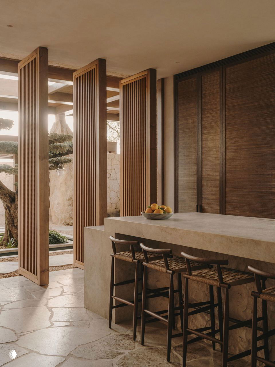 Кухонная зона с массивной бетонированной столешницей и высокими деревянными барными стульями на фоне раздвижных щитов — натуральные материалы и простые формы.