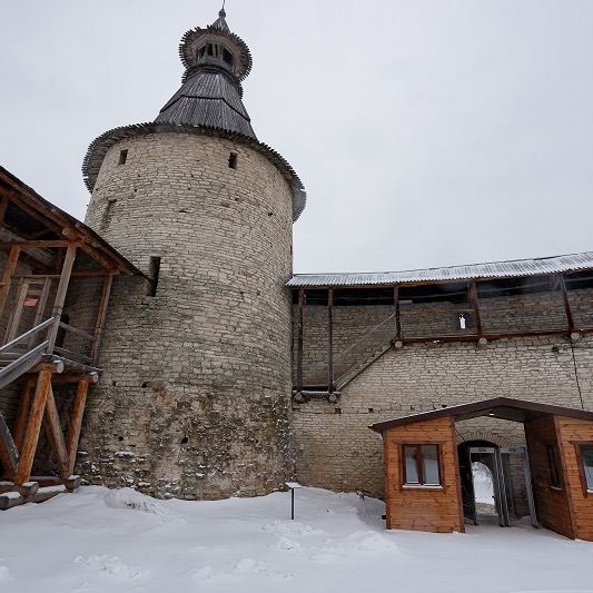 Каменная оборонительная башня Псковского кремля крупным планом, зимняя пора, видны элементы деревянной кровли и проход во двор.