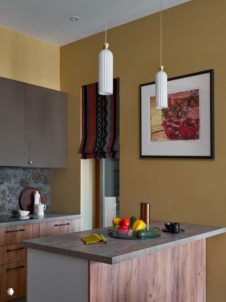 Кухонный остров с натуральной столешницей, на переднем плане яркие овощи и декоративные предметы, на стене — текстиль и картина в интерьере.