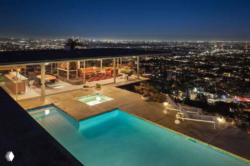 Общий вид на террасу, бассейн и ночной городской пейзаж — архитектурный силуэт Case Study House №22 с чётким горизонтальным навесом и видом на огни Лос‑Анджелеса.