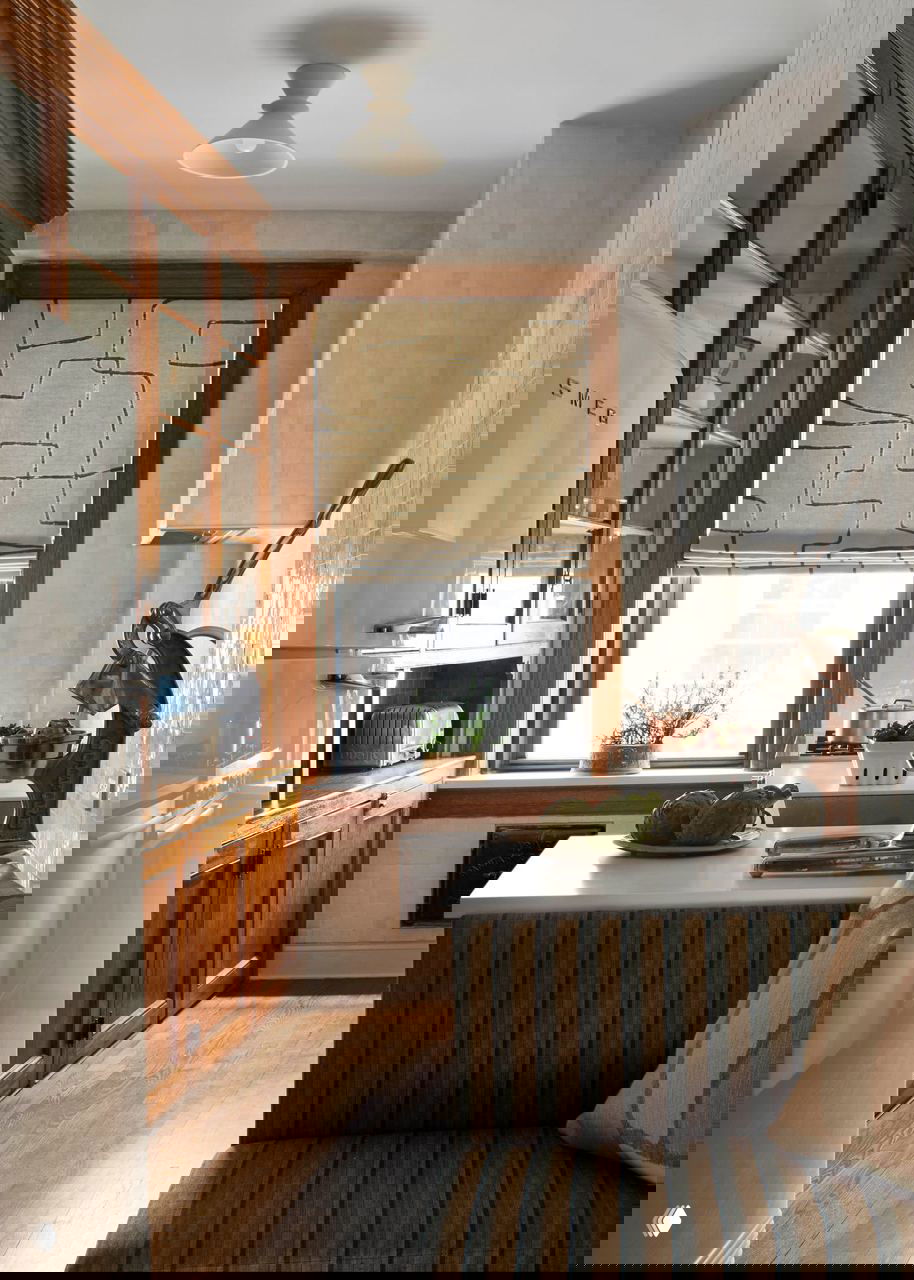 Кухонный интерьер: деревянные фасады, полосатая обивка углового дивана и небольшой белый стол у окна — сочетание старого и нового.