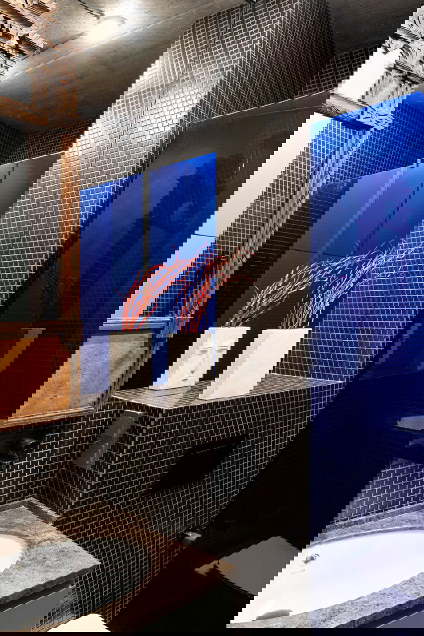 Санузел с маленькой черной мозаикой, синей стеклянной перегородкой душа и деревянной столешницей с раковиной — контрастные материалы и текстуры.