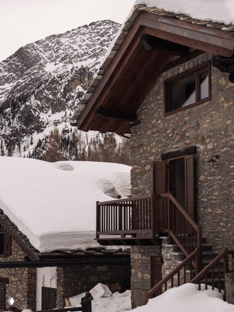 Фасад шале House Montagna в Курмайоре на фоне заснеженных склонов Монблана: каменная стена, балкон и глубокий снег вокруг.