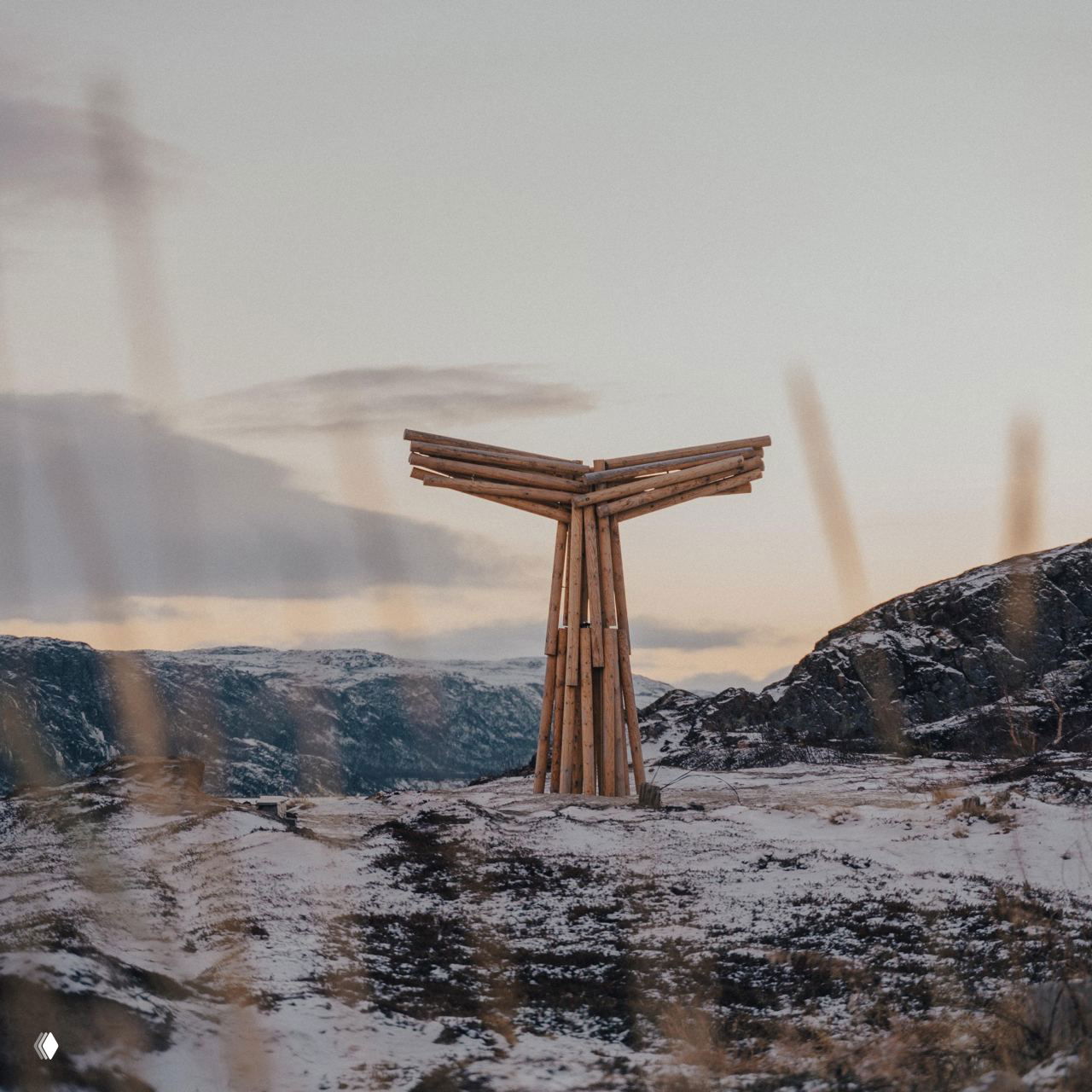 Деревянная инсталляция в форме хвоста кита на заснеженном пригорке Териберки; минималистичная арт-структура на фоне скал и неба.