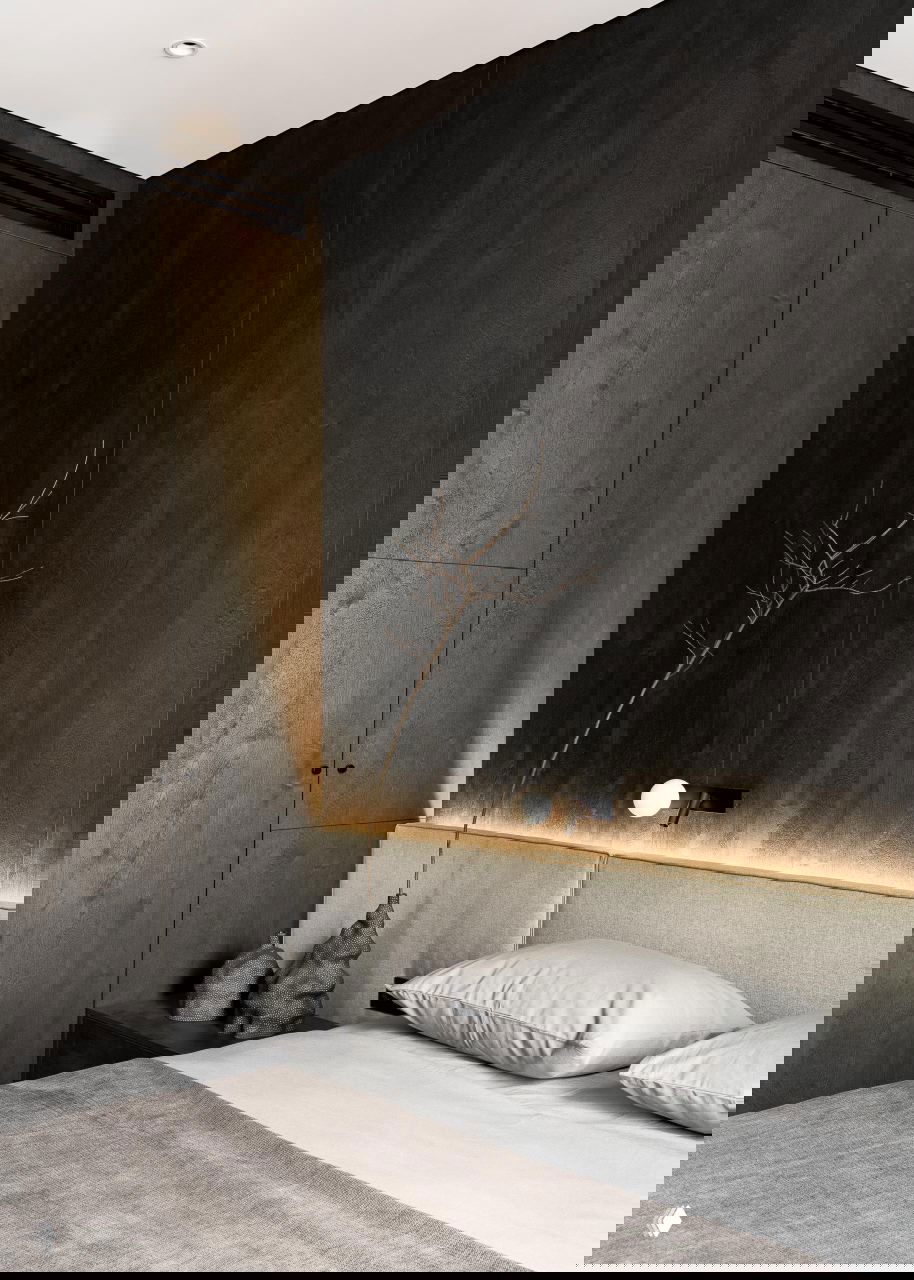 Крупный план спальни: серая постель, текстурные тёмные панели и минималистичные прикроватные элементы декора.