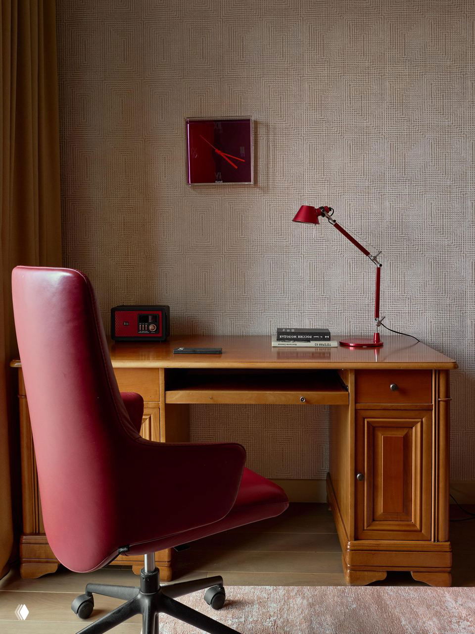Рабочая зона: деревянный классический стол и бордовый офисный стул, настольная лампа и минималистичный набор аксессуаров на фоне текстурных обоев.