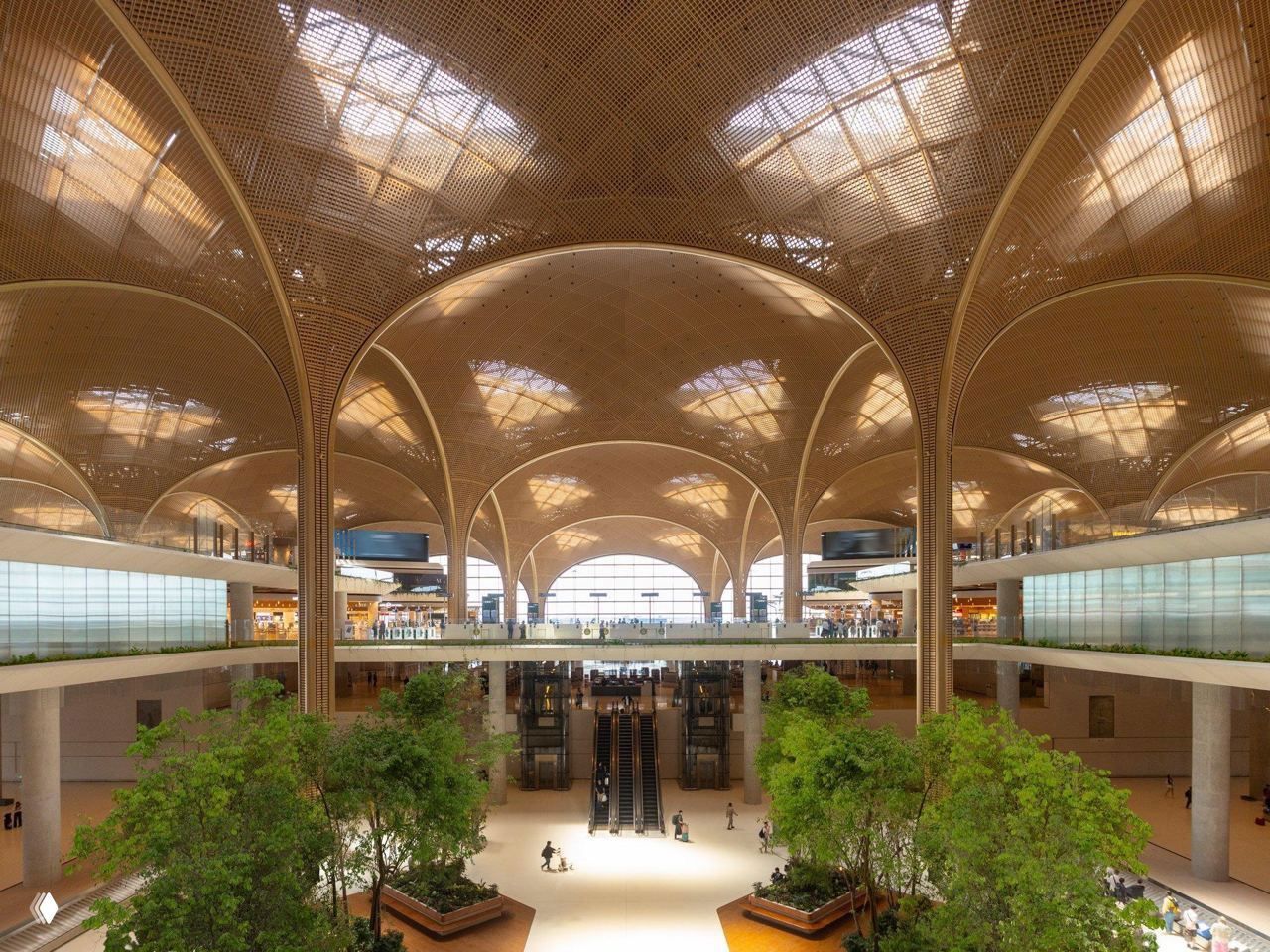 Интерьер главного зала аэропорта с высокими арками и изогнутыми сводами из решетчатых панелей, дневной свет и зеленые растения у входа.
