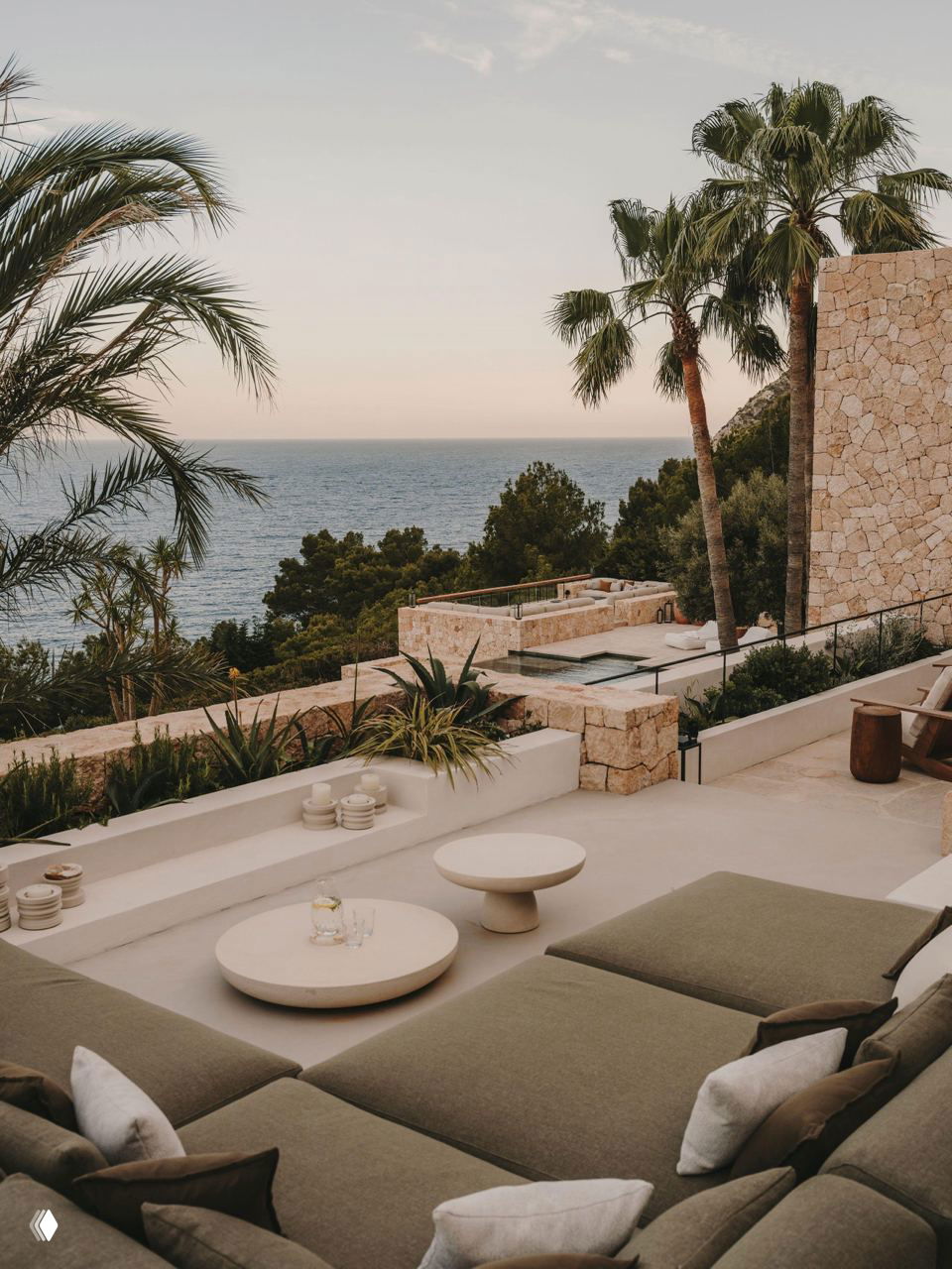 Вид с террасы на море и пальмы: каменные стены, открытые зоны отдыха и ступенчатая архитектура участка, вписанная в средиземноморский пейзаж.