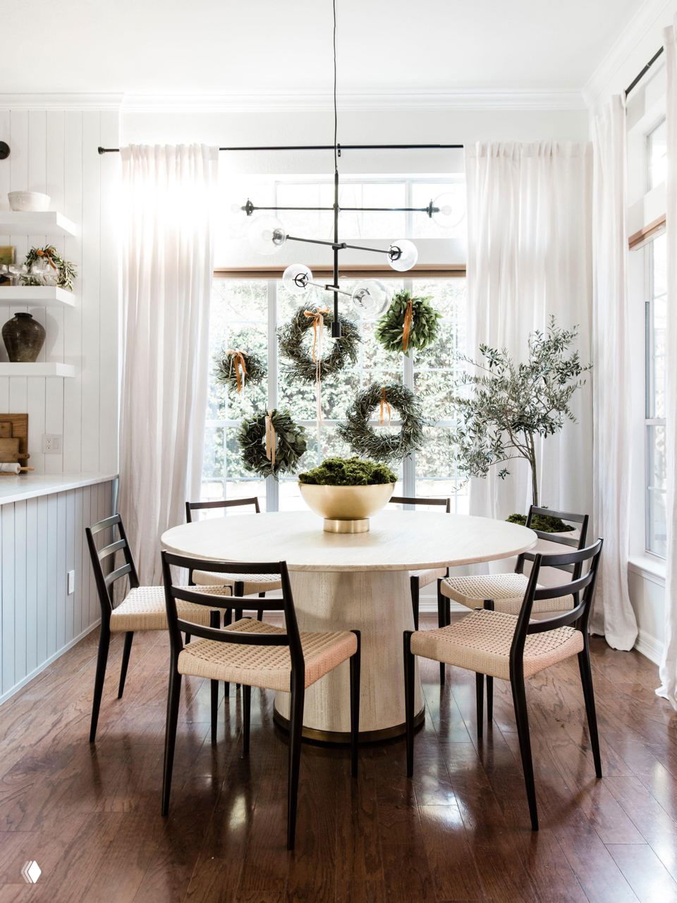 Светлая столовая у большого окна с несколькими венками на стекле, белыми занавесками и минималистичным декором в скандинавском стиле интерьера.
