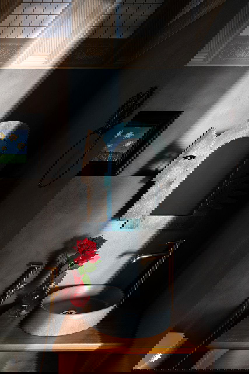 Малый туалет или умывальник с бетонной раковиной, деревянной тумбой и солнечным лучом, падающим на зеркало и красную розу в вазе.