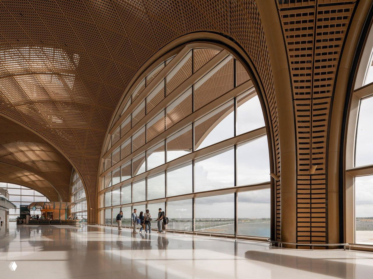Коридор возле больших арочных окон: пассажиры идут вдоль стеклянного фасада, видна ритмичная решетчатая структура крыши и отражения на полу.