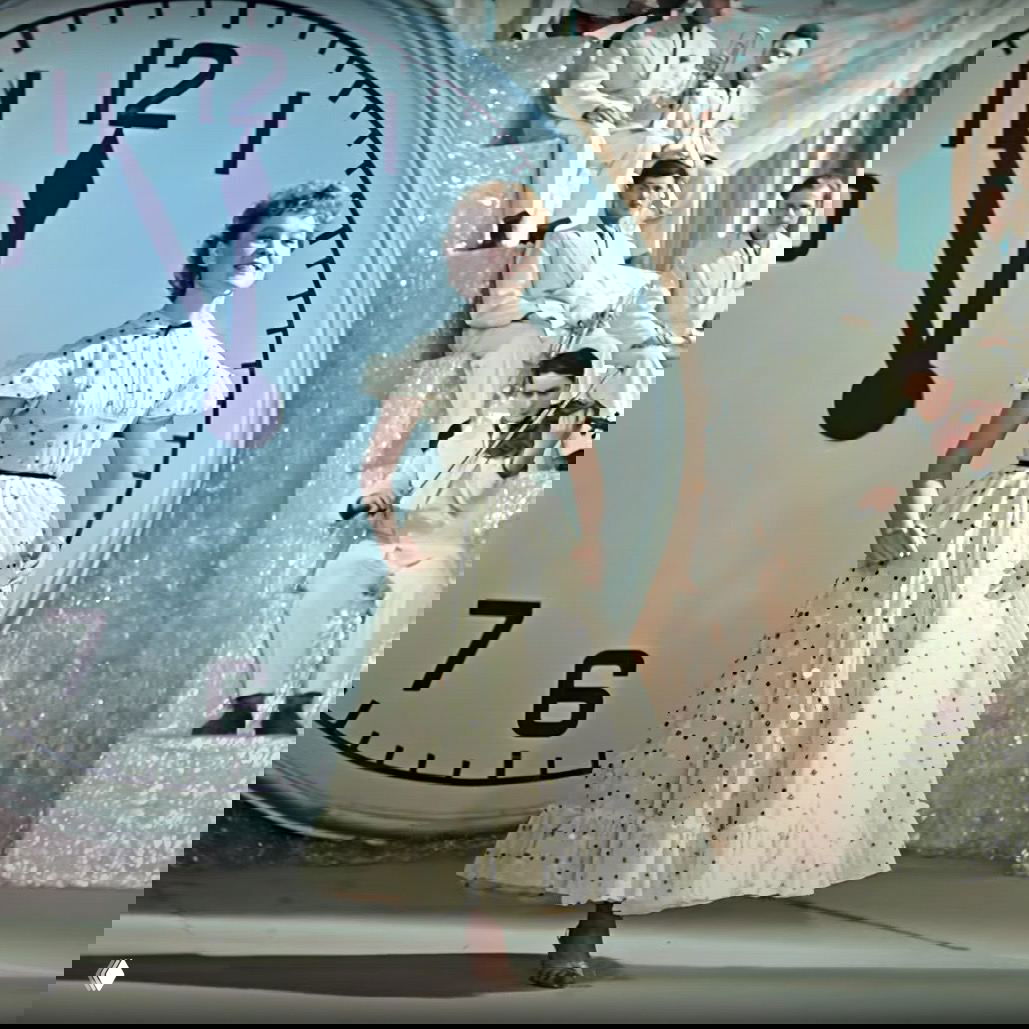 Танцевальная сцена на фоне большого циферблата часов — праздничная постановка с оркестром и сценографией, ассоциирующаяся с новогодним шоу.