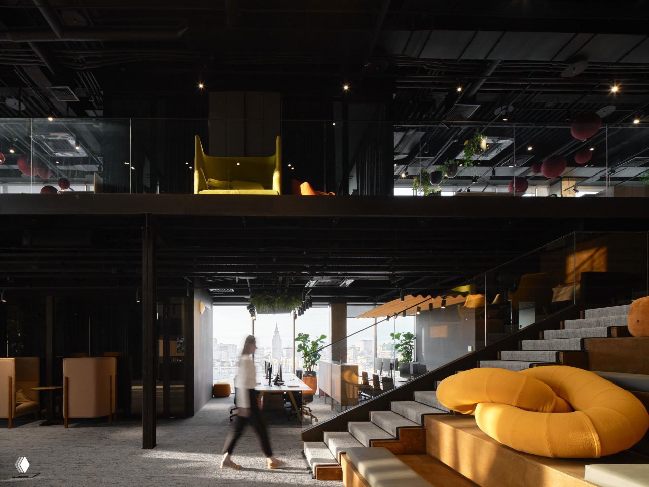 Двухуровневый офис с переходом через лестницу, стеклянными перилами и видом на городской пейзаж; на переднем плане — крупный жёлтый пуф и сидения.