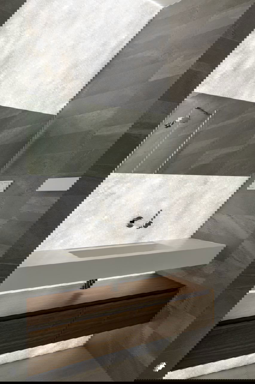 Санузел с подвесной столешницей и подсветкой декоративного камня за зеркалом, монохромная плитка и минималистичная сантехника создают эффект чистоты и глубины.