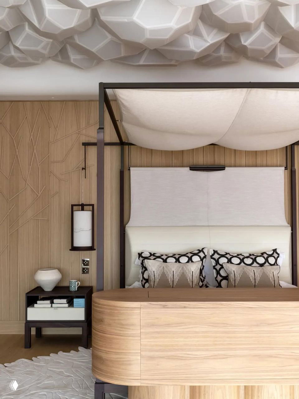 Спальня с текстурированным белым потолком и светлой деревянной мебелью, мягкие формы кровати создают спокойную атмосферу и акцент на небе комнаты.