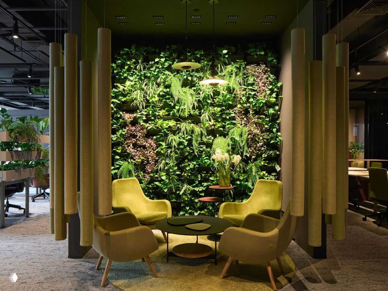 Уютный уголок для переговоров с зелёной вертикальной стеной из растений, мягкими креслами оливкового тона и низкими столиками на фоне офисного пространства.