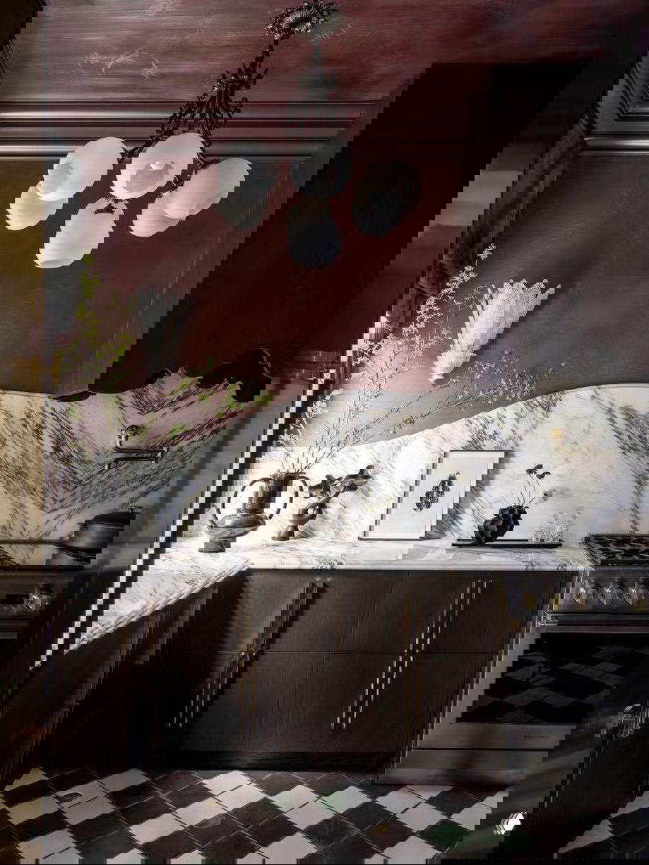 Кухонный интерьер с глубоким бардовым потолком и мраморной столешницей, тёмные шкафы и декоративный фартук усиливают эффект акцента сверху.