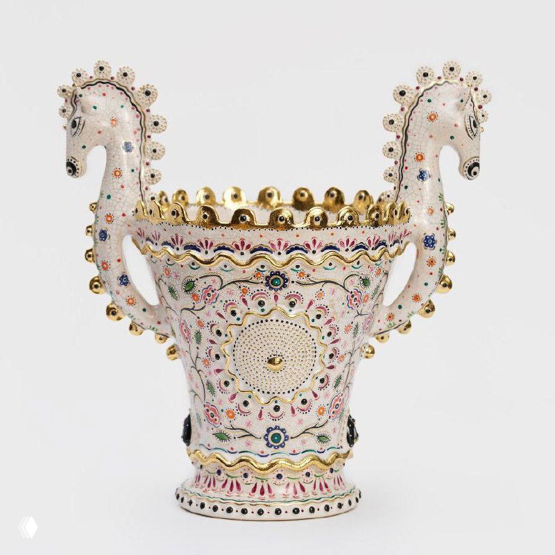Две стилизованные головки коней, выступающие в виде ручек вазы или ритуального ритона, белая керамика с цветной росписью и золотом.