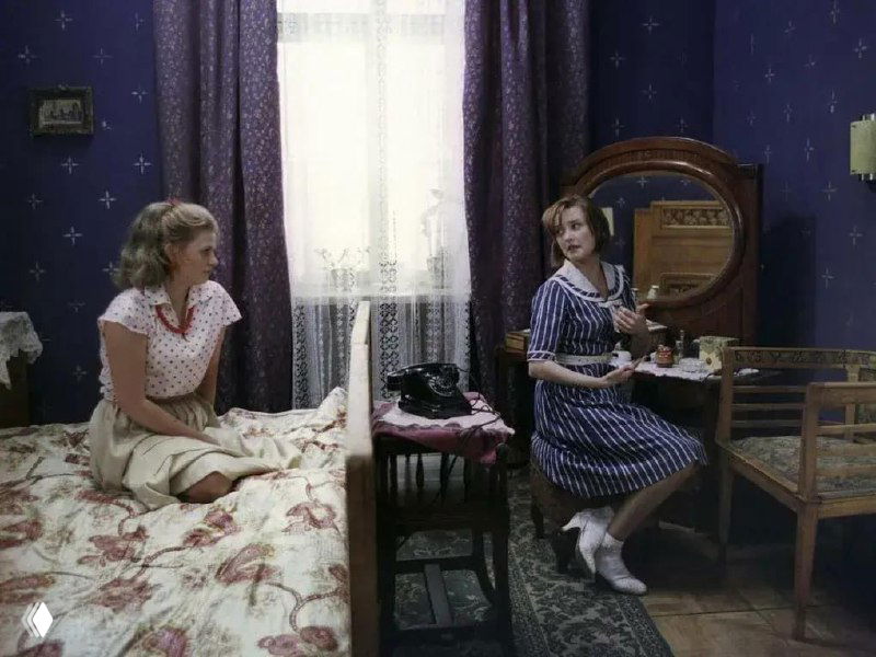 Комната с двумя кроватями, тёмно-синими обоями, старым телефоном на тумбочке и женщинами в одежде середины XX века — кадр из фильма.