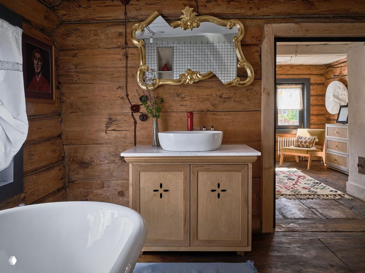 Раковина и зеркало в интерьере дома: декоративное золочёное зеркало на фоне тёплого деревянного сруба и мебели из светлой древесины.