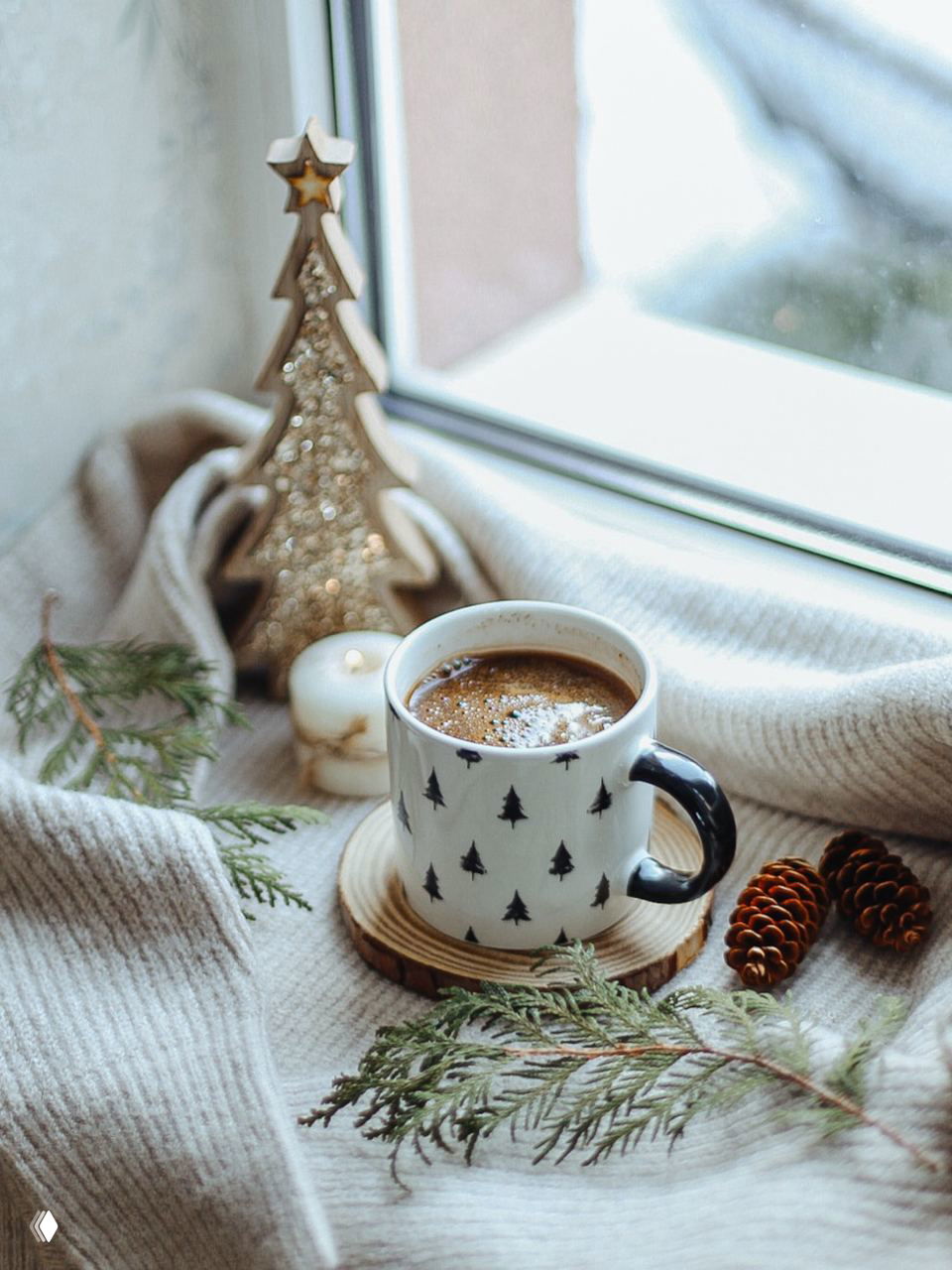 Уютная композиция у окна: тёплый плед, кружка кофе, декоративные шишки и веточки — кадр для атмосферы домашнего ожидания праздника в холодный сезон.