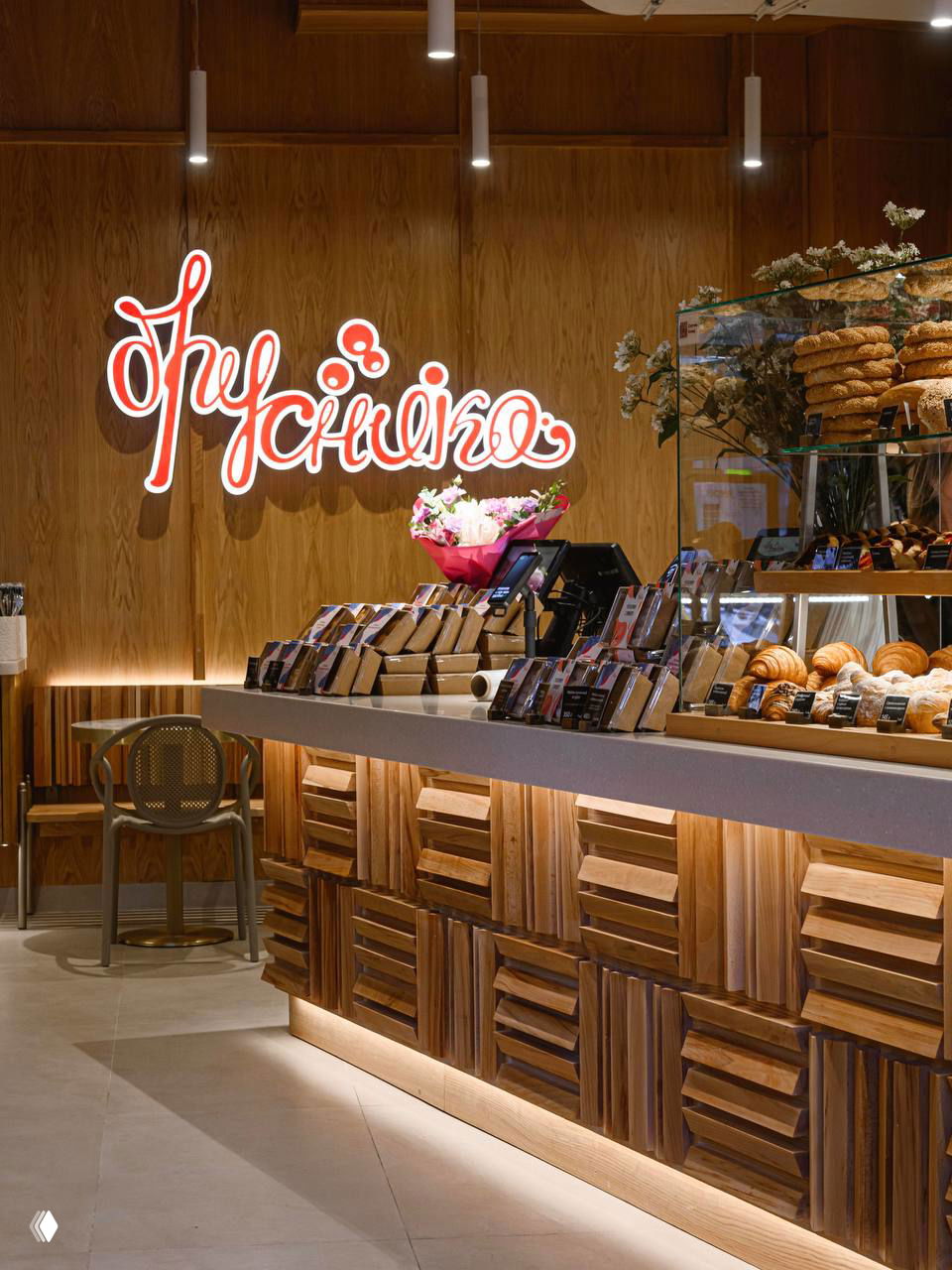 Деревянная барная стойка кафе «Брусника» с подсветкой, витрина с булочками, неоновая вывеска бренда и тёплая атмосфера интерьера.