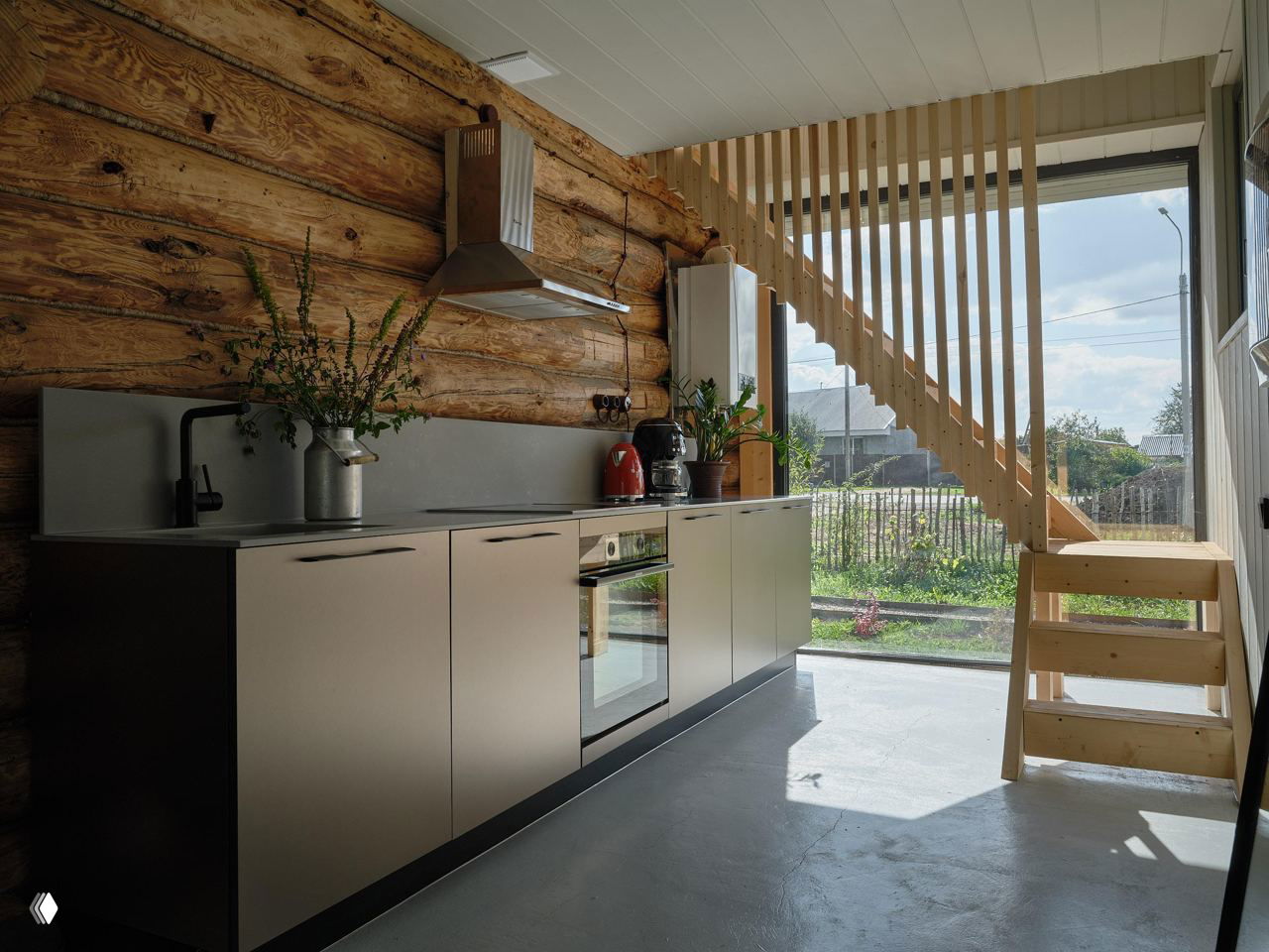 Кухонная зона в доме Менчакова: современная кухня и большой стеклянный фасад, выходящий в сад, сочетаются с бревенчатыми стенами.