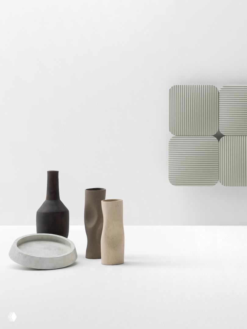 Четырёхмодульная секция радиатора Lana светло-серого цвета на белой стене рядом с каменными вазами и минималистичным столом в светлом оформлении.