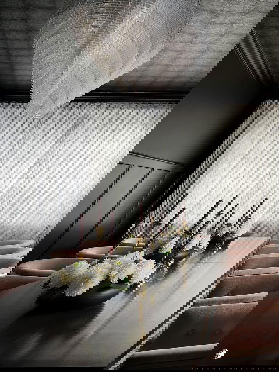 Столовая с широкой обеденной зоной и тёмным потолком с текстурой, длинный стол и люстра подчёркивают силуэт помещения и делают потолок центром внимания.