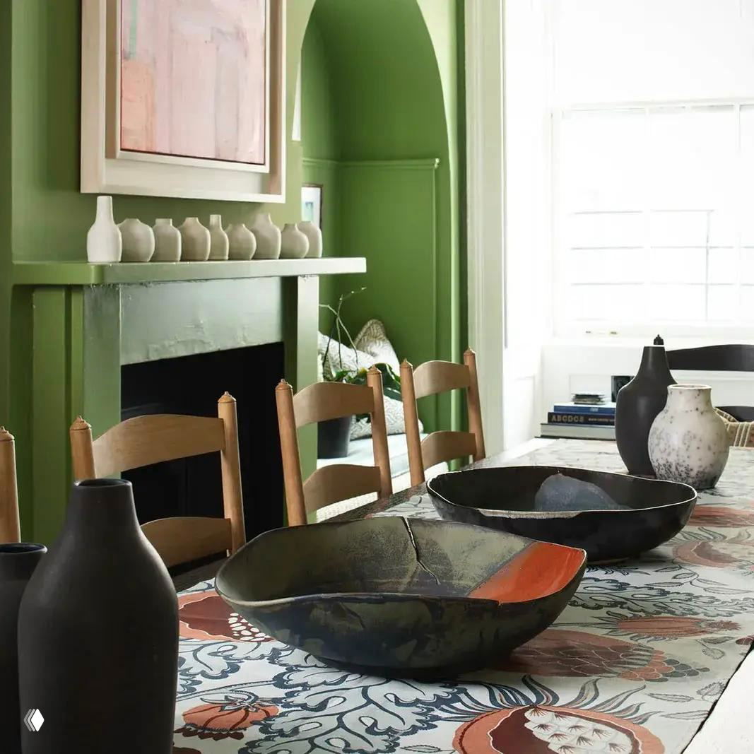 Домашняя столовая сцена: стол с керамическими мисками и вазами на фоне зелёного камина и арочной ниши — интерьерный снимок с акцентом на текстуру.