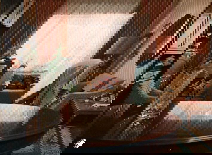 Гостиная в представительной квартире: круглый стол, мягкая мебель, шторы и женщина, наводящая порядок — образ «генеральского» жилища.