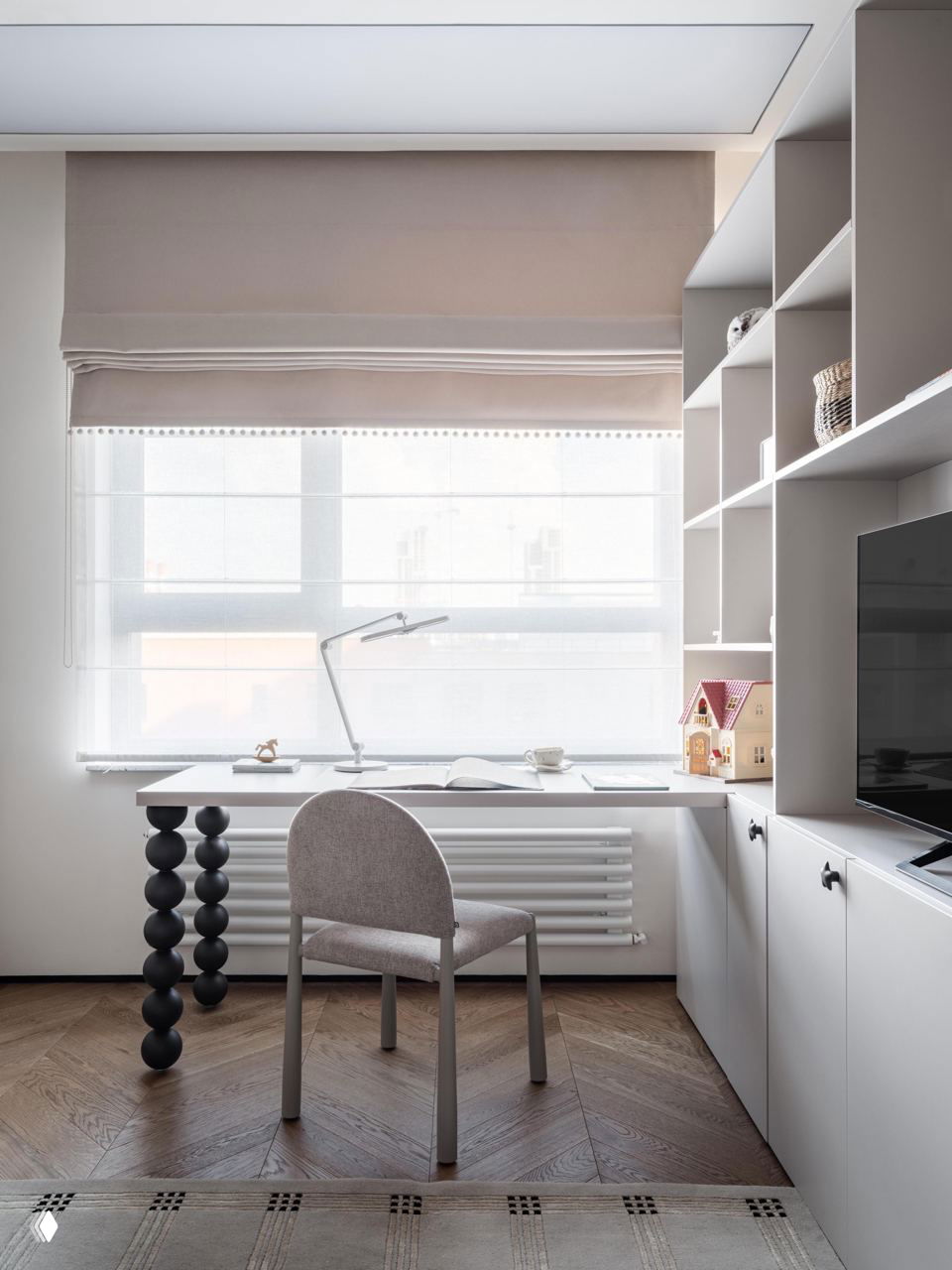 Рабочее место у окна с функциональным столом, встроенными стеллажами и паркетом «ёлочкой»; естественный свет подчёркивает спокойную нейтральную гамму интерьера.