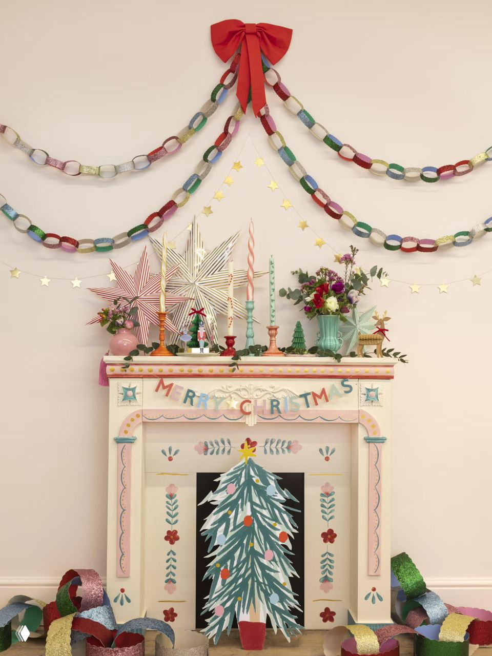 Нежный пастельный камин, украшенный бумажной елкой, гирляндами и свечами; декоративные звезды, цветы и мелкие детали создают сказочную композицию.