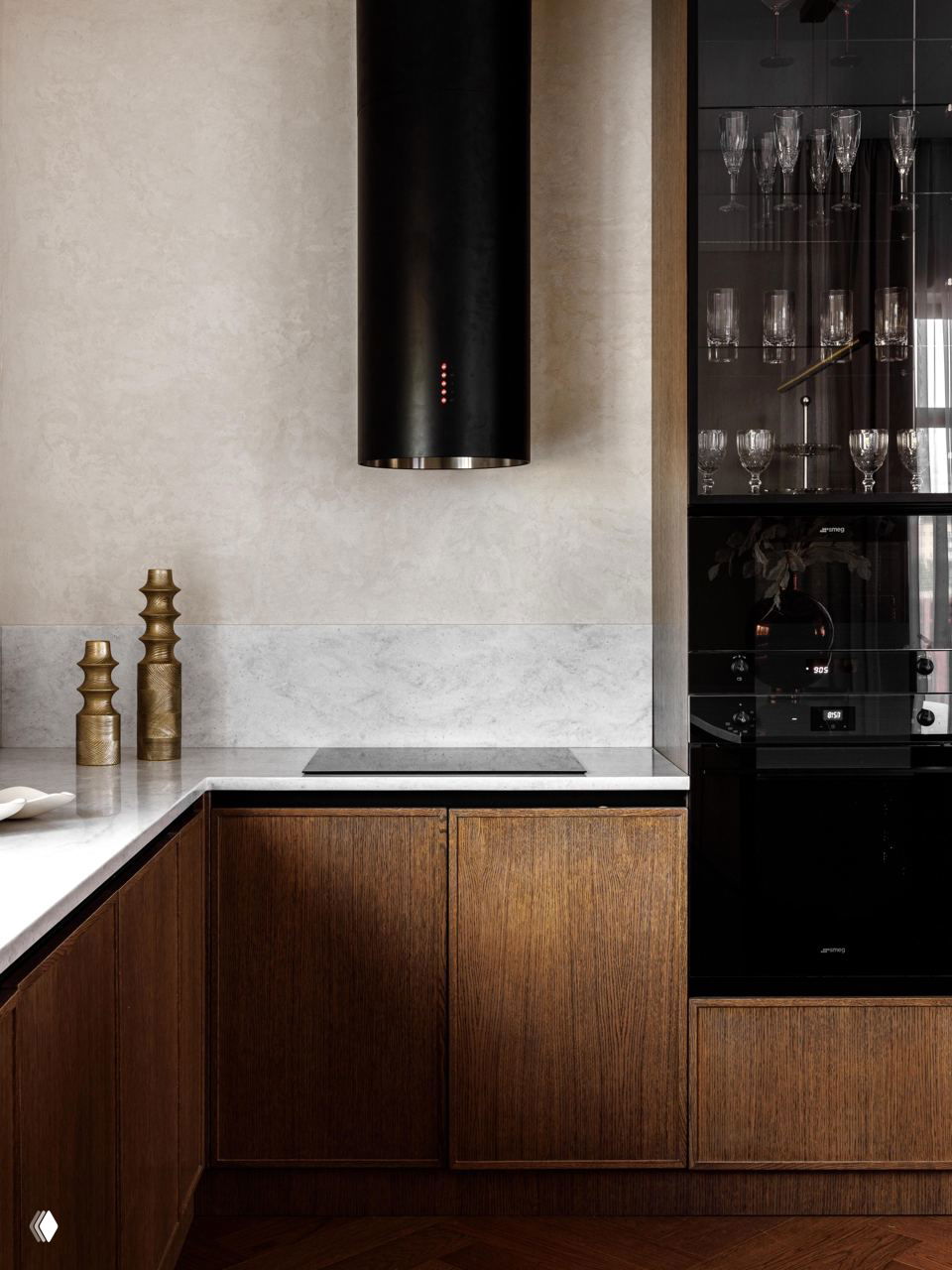 Кухонная зона с мраморной столешницей, деревянными фасадами шкафов и тёмной цилиндрической вытяжкой на фоне спокойной бежево-коричневой отделки.