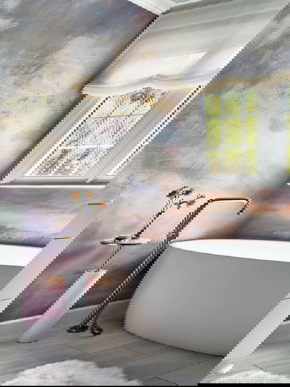 Ванная комната с отдельно стоящей овальной ванной на фоне художественной мраморной стены и большим окном, через которое видна зелень сада, акцент на материалы и спокойствие.