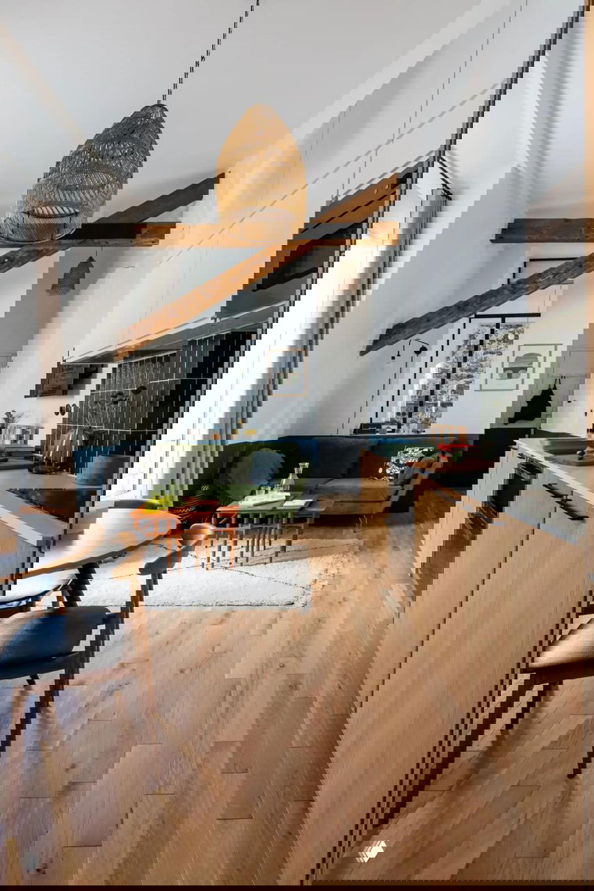 Кухня‑гостиная в небольшой парижской квартире: светлый интерьер с деревянными балками, деревянным полом, зелёным диваном и тёмно‑синей нижней покраской стен.