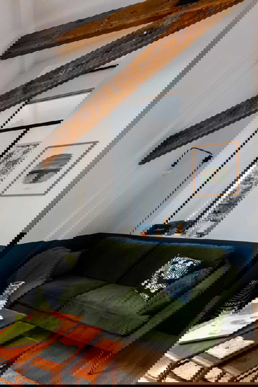 Уютный уголок с тёмно‑зелёным диваном и низкими деревяными столиками, на фоне темно‑синей ленточной покраски стен и декоративных деревянных балок под потолком.